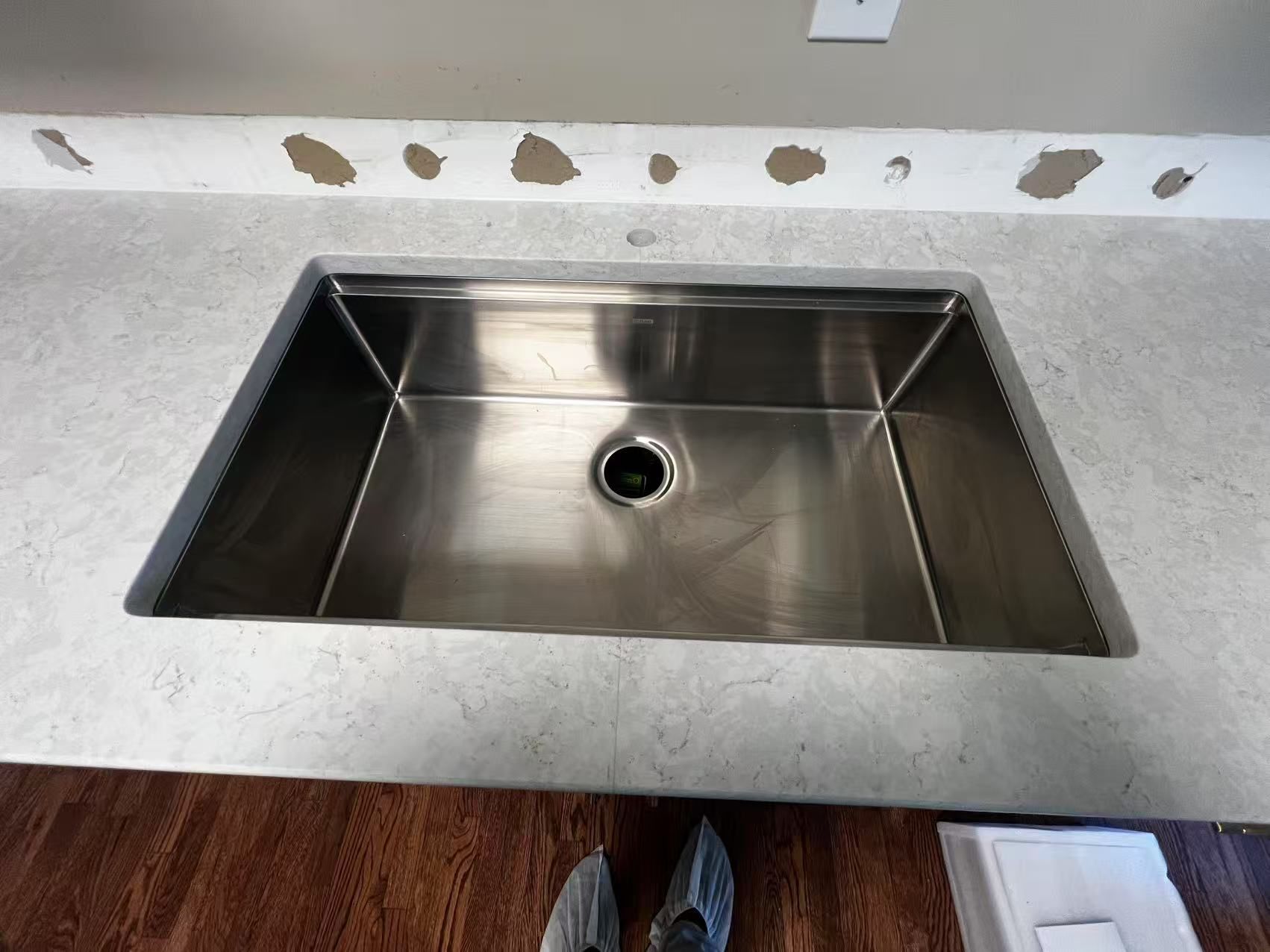 A person is standing in front of a stainless steel kitchen sink.