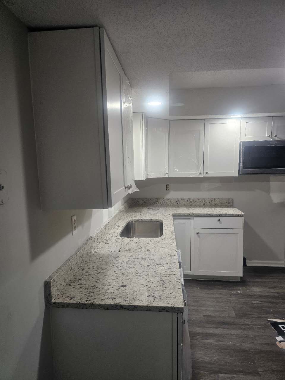 A kitchen with white cabinets, granite counter tops, a sink, and a microwave.