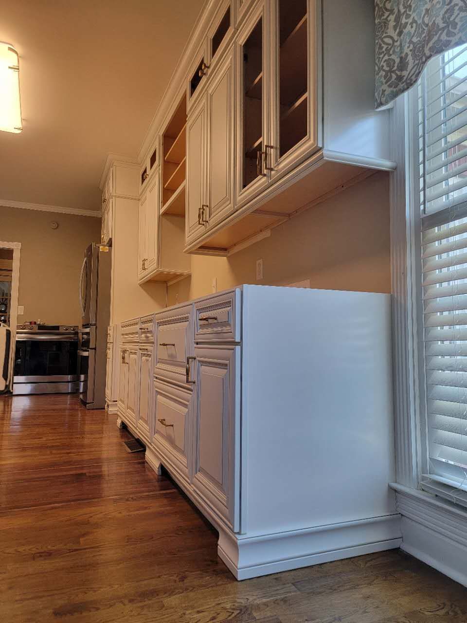A kitchen with white cabinets and a window with blinds.