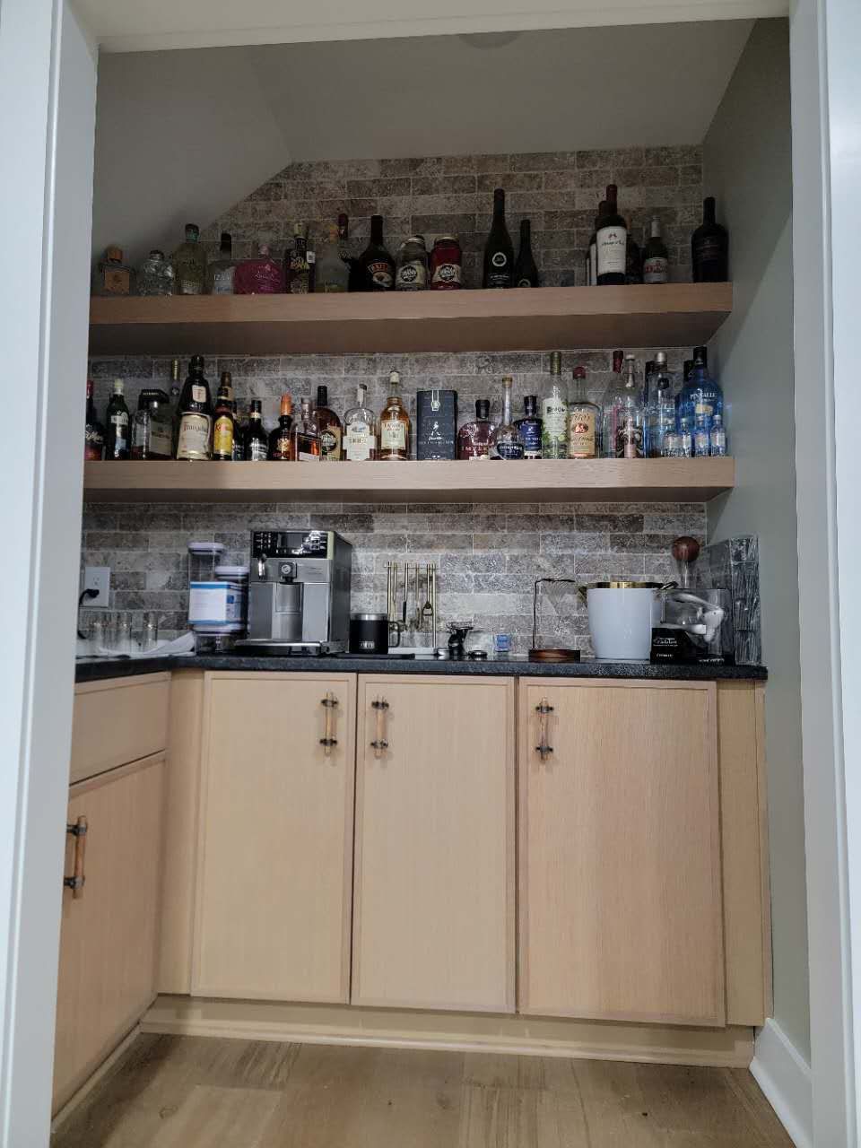 A kitchen with wooden cabinets and shelves filled with bottles of alcohol.