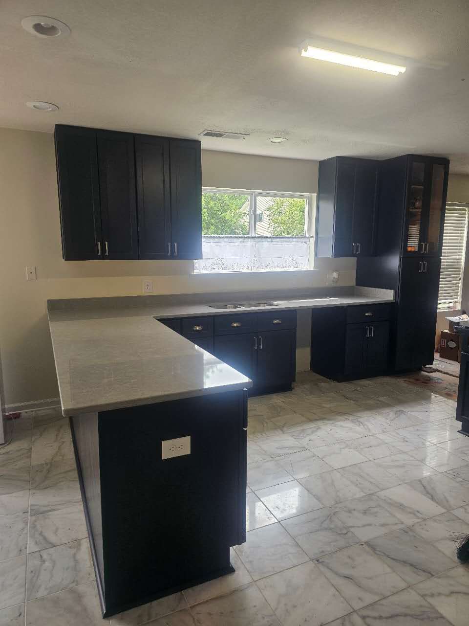 A kitchen with black cabinets and a marble counter top.