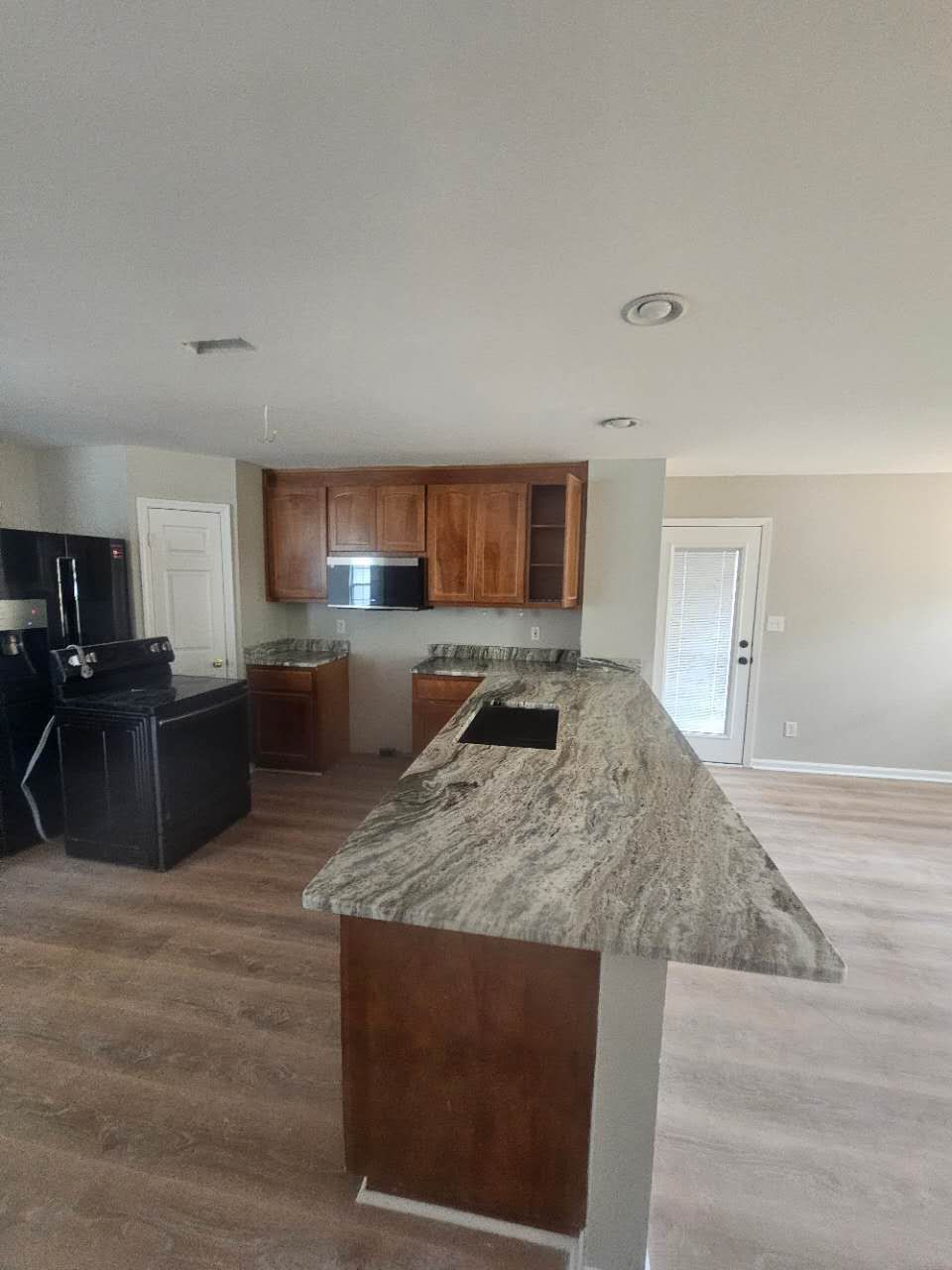 A kitchen with granite counter tops, wooden cabinets, and a black refrigerator.