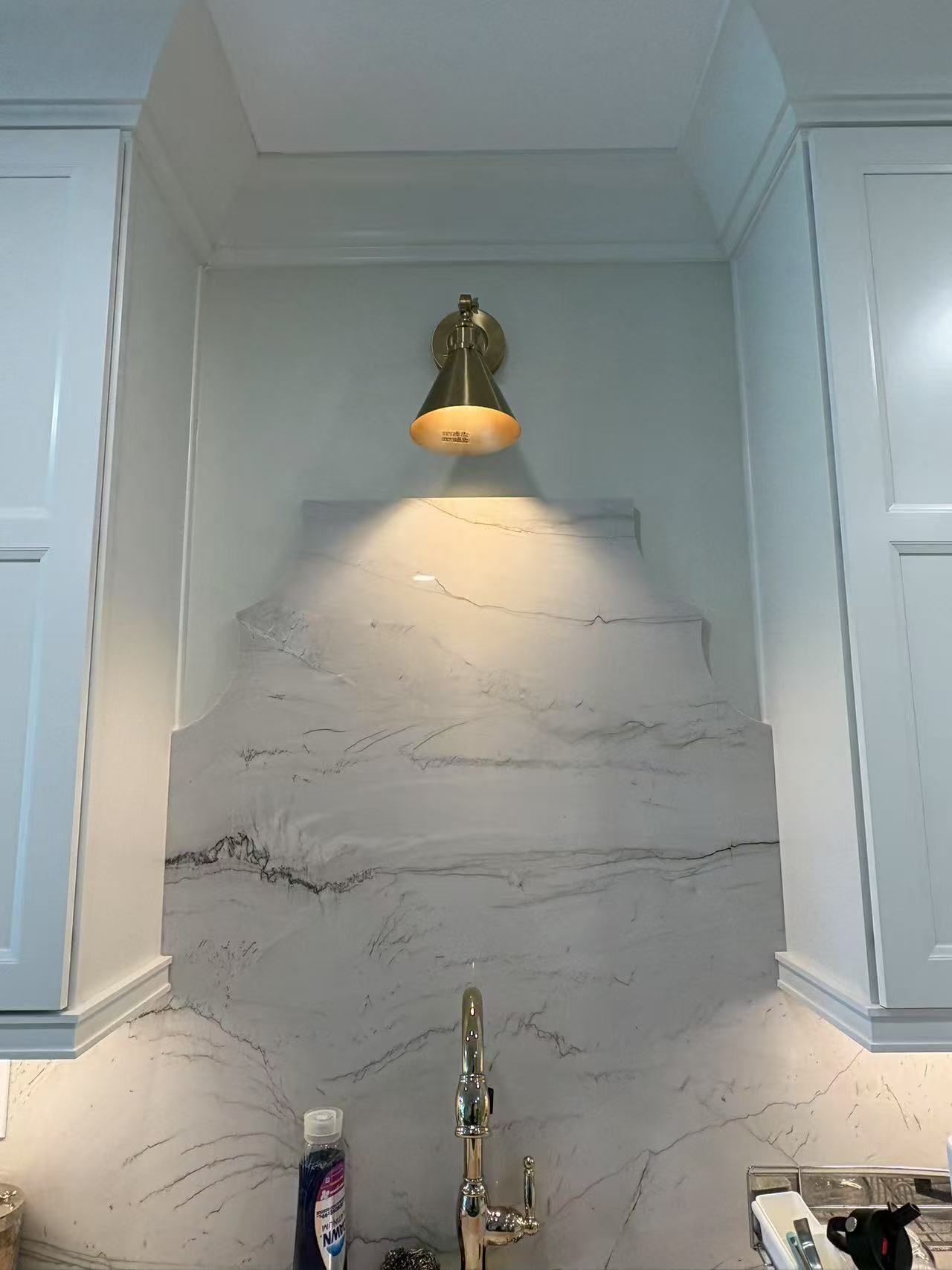 A kitchen sink with a light on the wall above it.