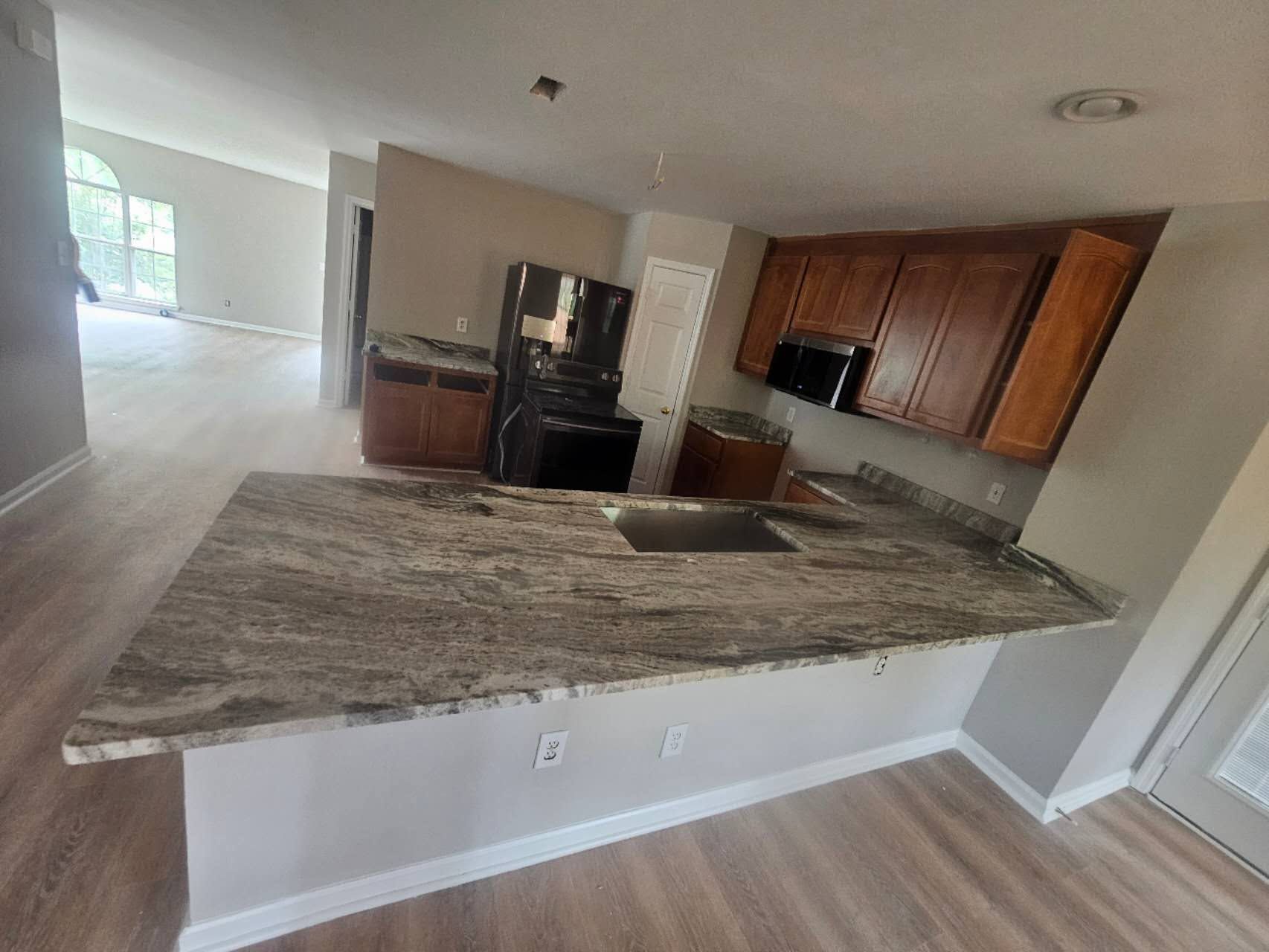 A kitchen with granite counter tops, wooden cabinets, a refrigerator, and a sink.