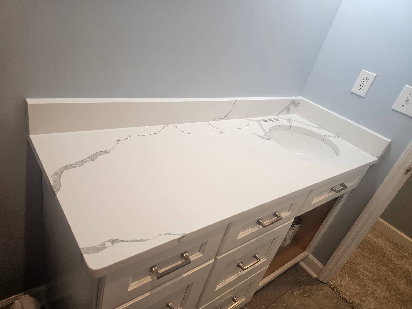A bathroom vanity with a white counter top and a sink.