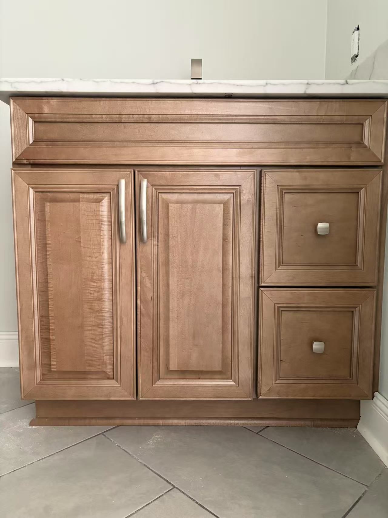 A bathroom vanity with wooden cabinets and drawers and a marble counter top.