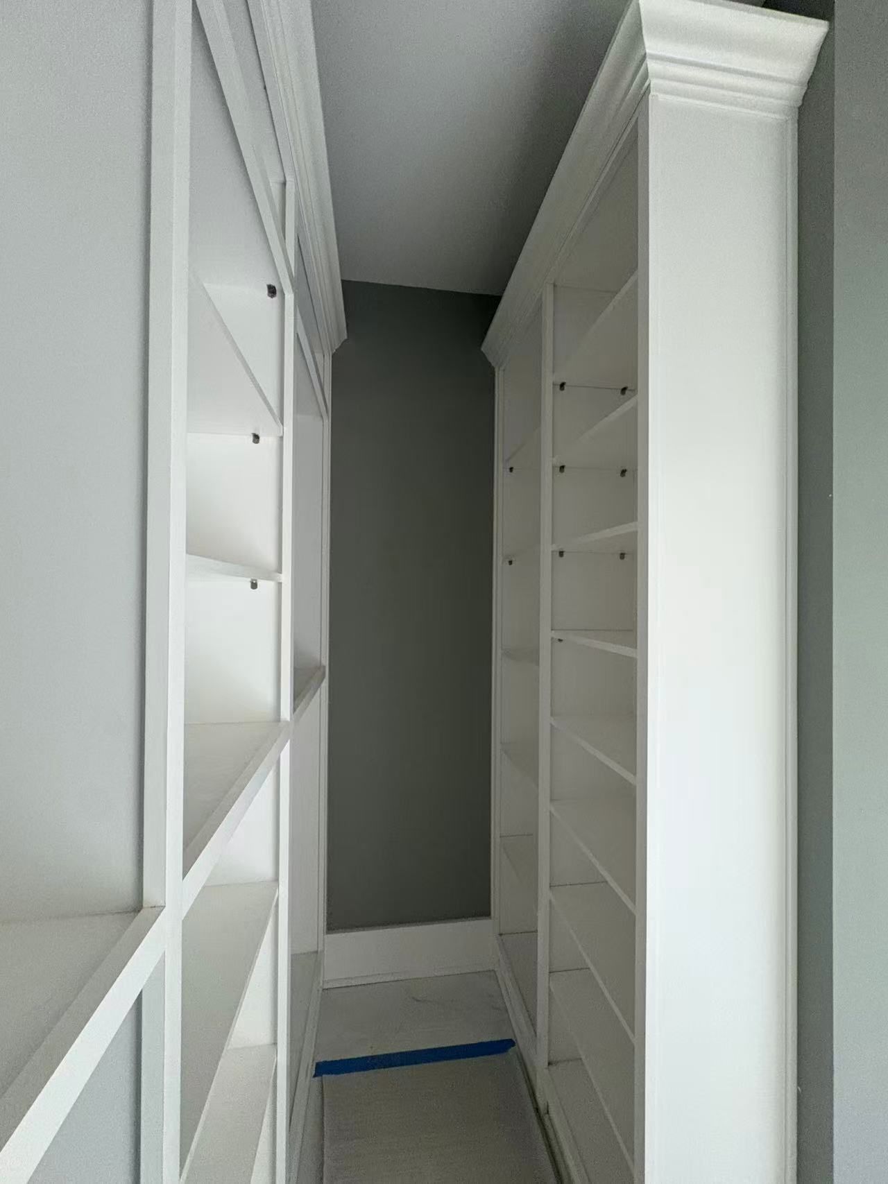 A narrow, built-in shelving space or closet with white shelving units on both sides.