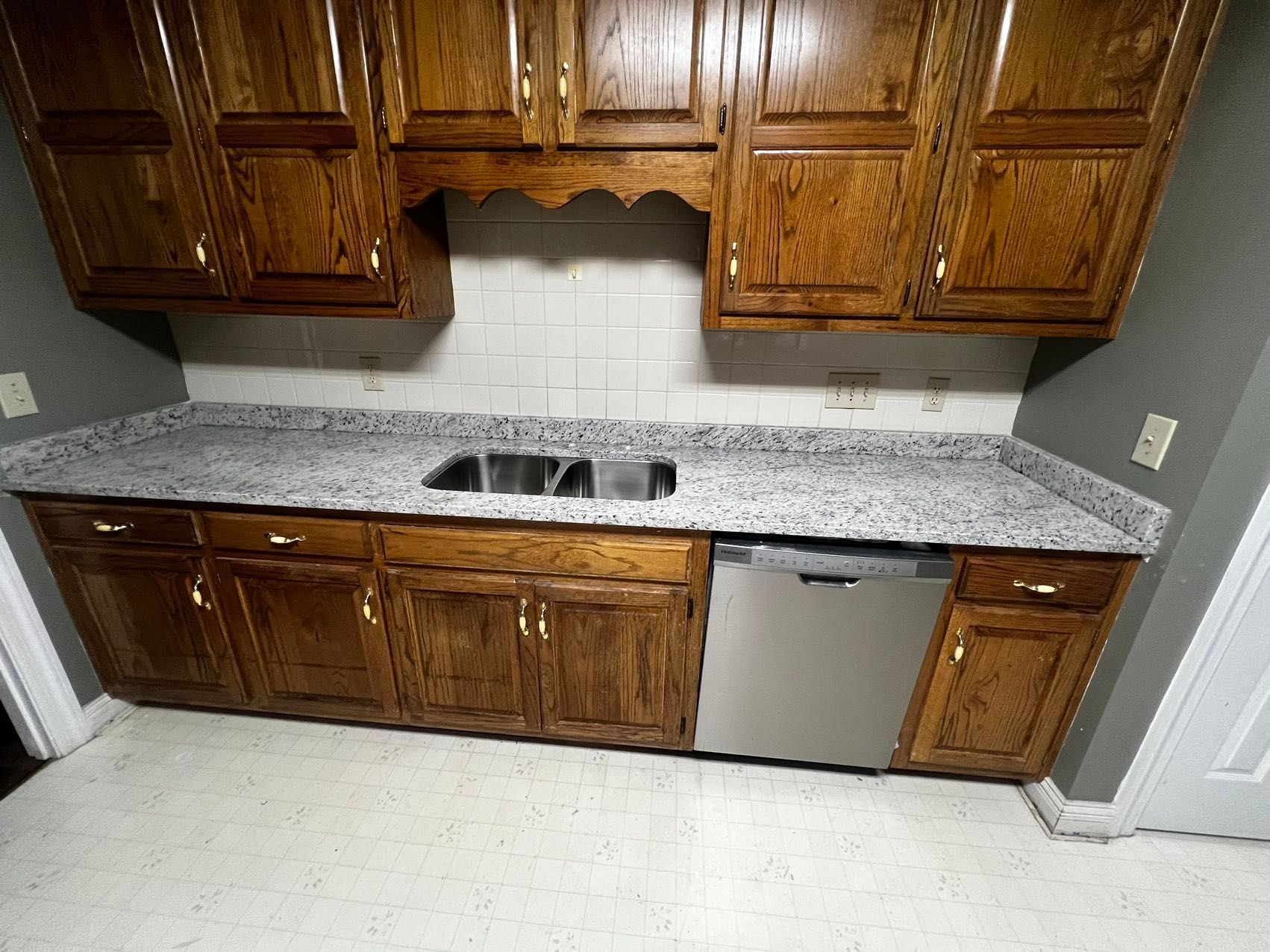 A kitchen with wooden cabinets, granite counter tops, a sink, and a dishwasher.