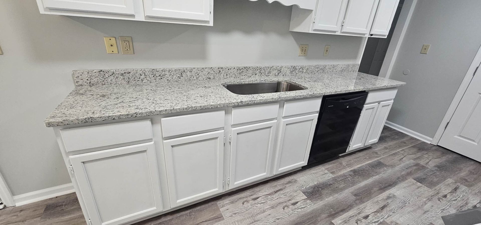 A kitchen with white cabinets, granite counter tops, a sink, and a dishwasher.