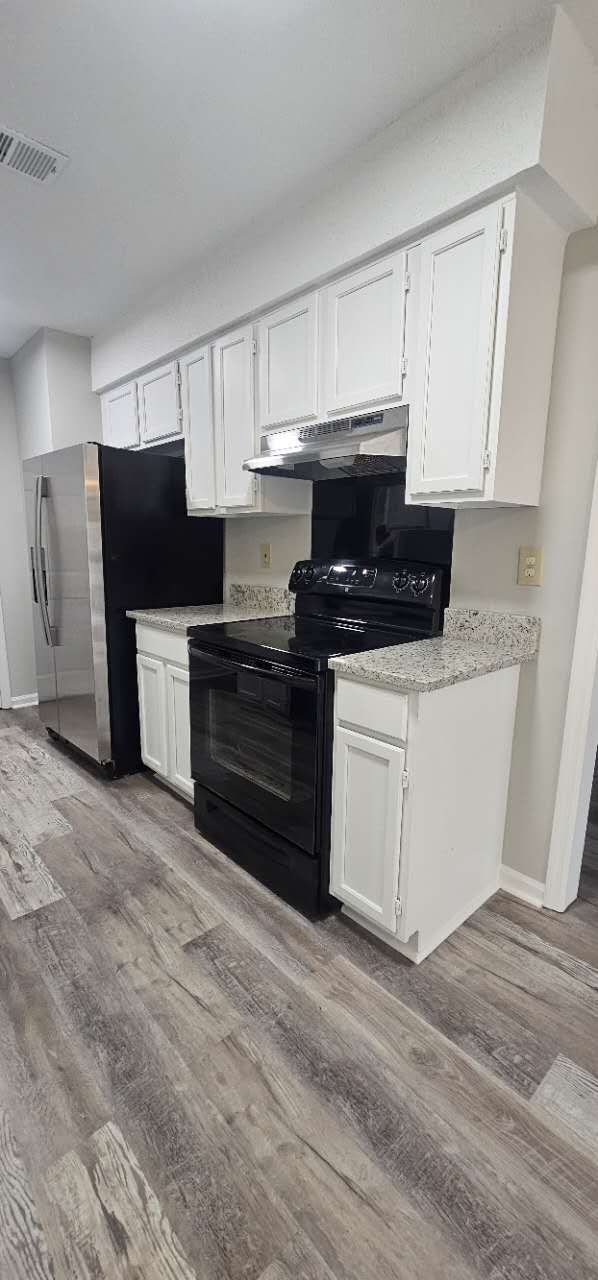 A kitchen with white cabinets, black appliances, and a refrigerator.