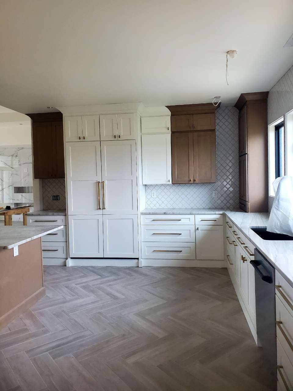 A kitchen with white cabinets and brown cabinets and a herringbone floor.