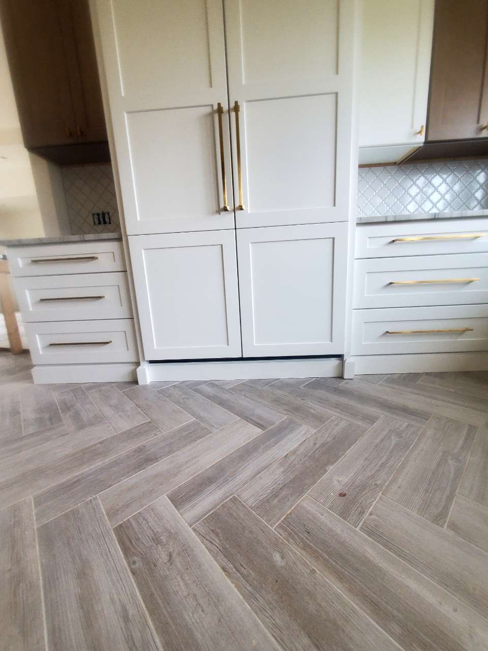 A kitchen with white cabinets and a herringbone floor.