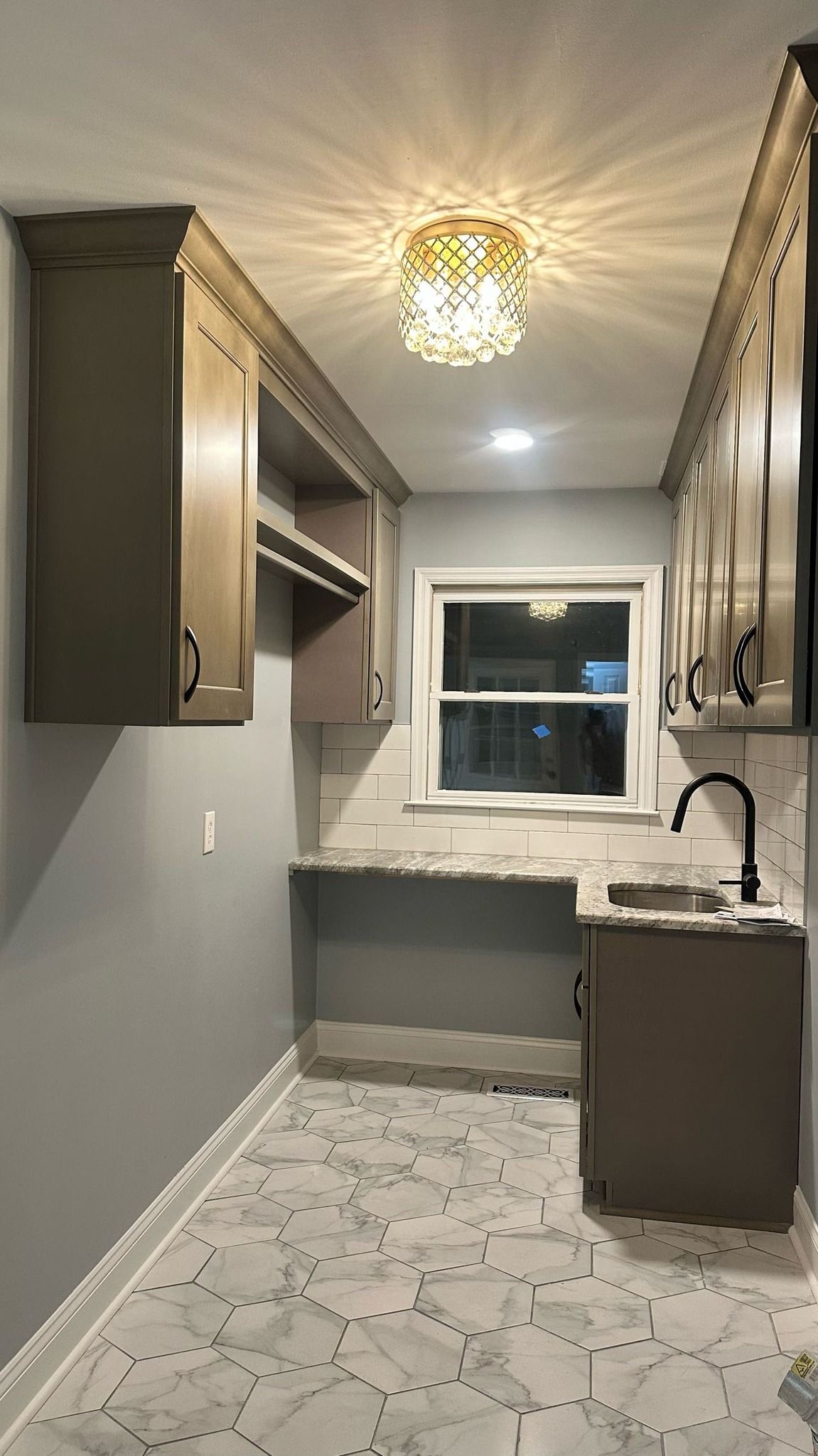 A laundry room with a sink, cabinets, and a window.