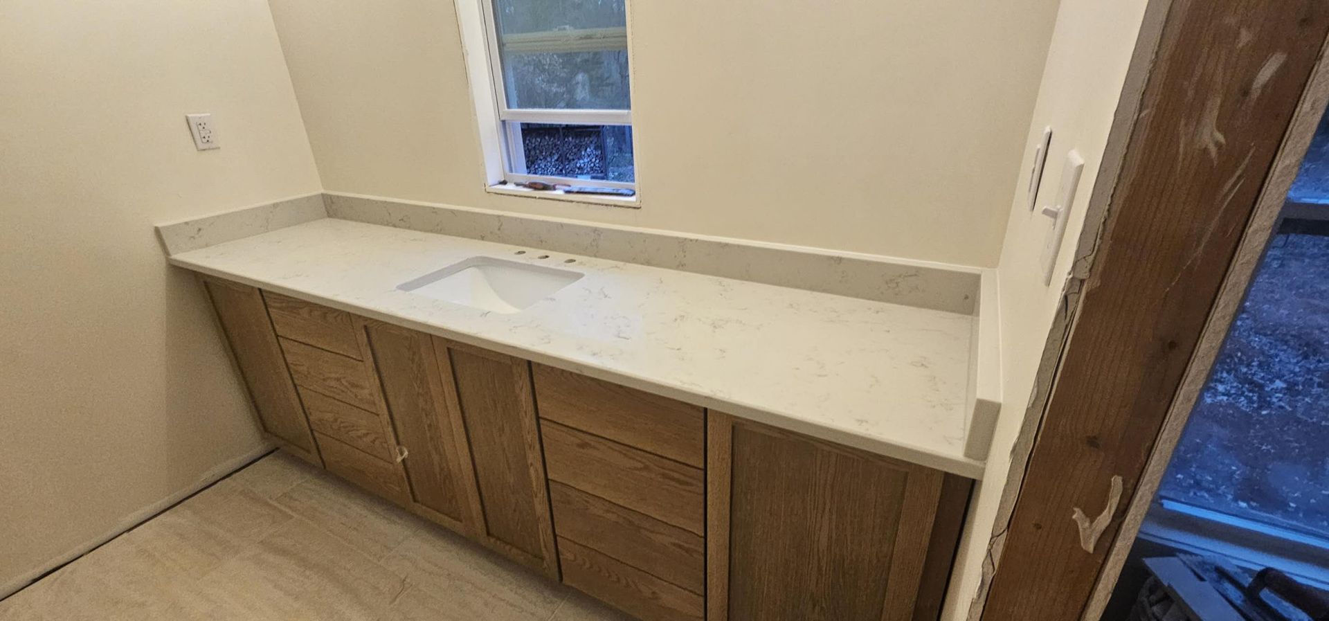 A bathroom with a sink, cabinets, and a window.
