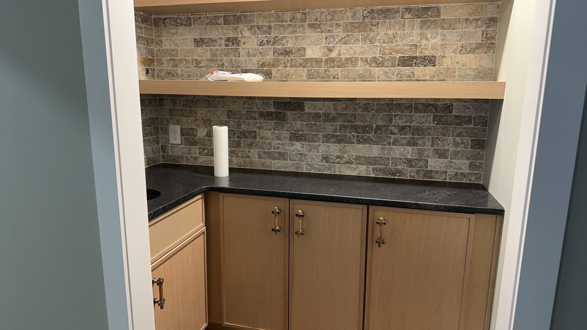 A kitchen with wooden cabinets, granite counter tops, and a brick wall.