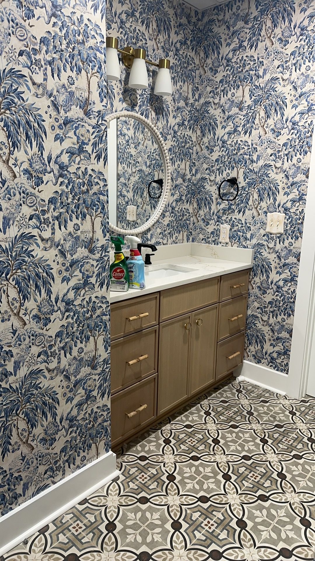 A bathroom with a sink, mirror, and blue and white wallpaper.