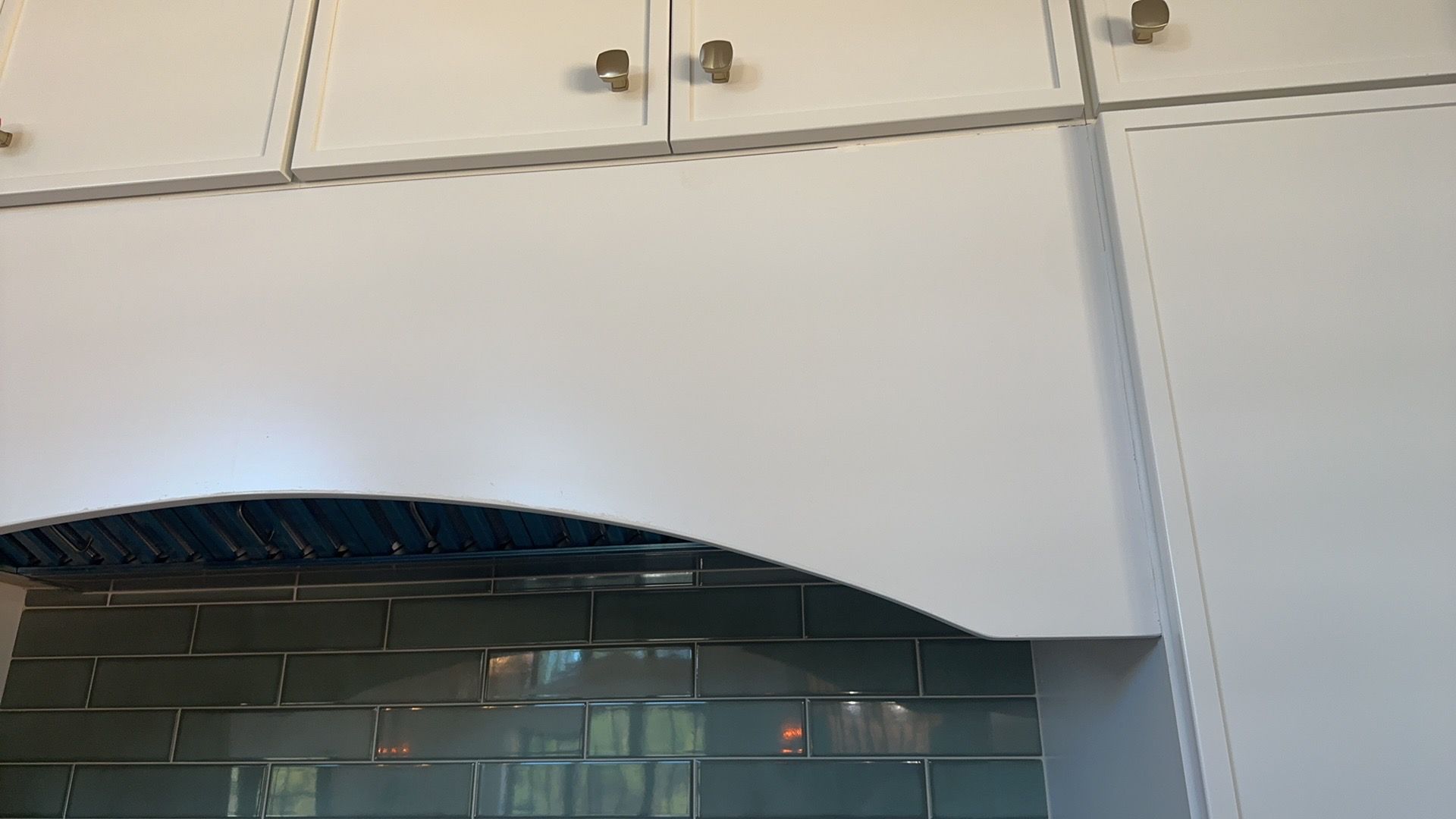 A kitchen with white cabinets and a hood above the stove.