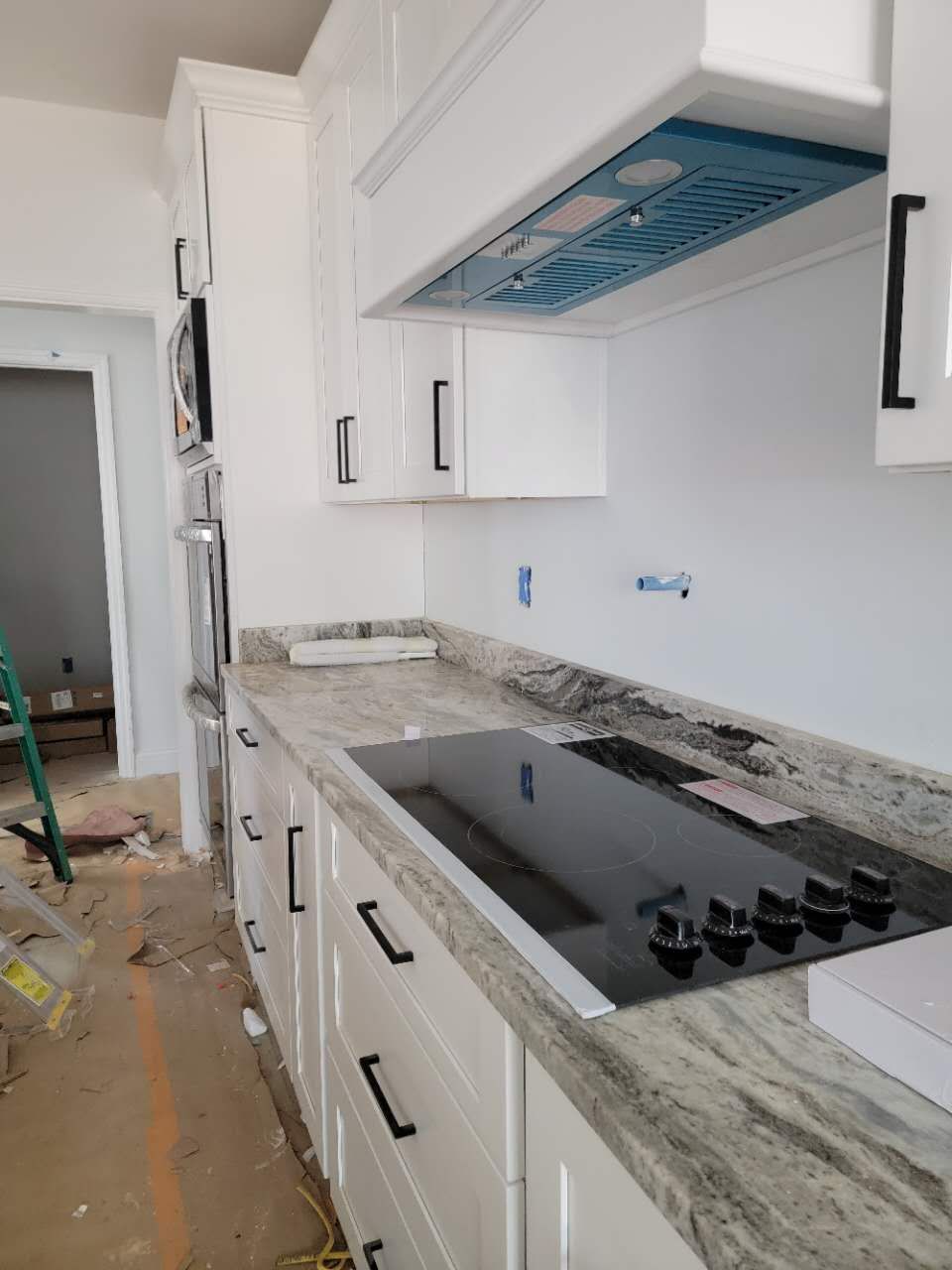 A kitchen with white cabinets, granite counter tops, and a stove top oven.