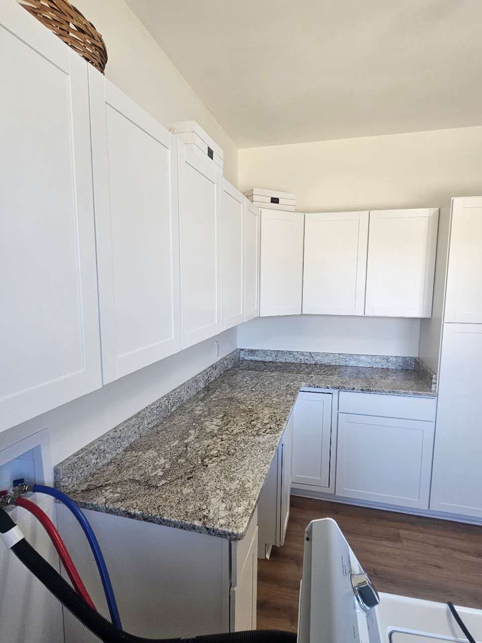 A laundry room with white cabinets and granite counter tops.