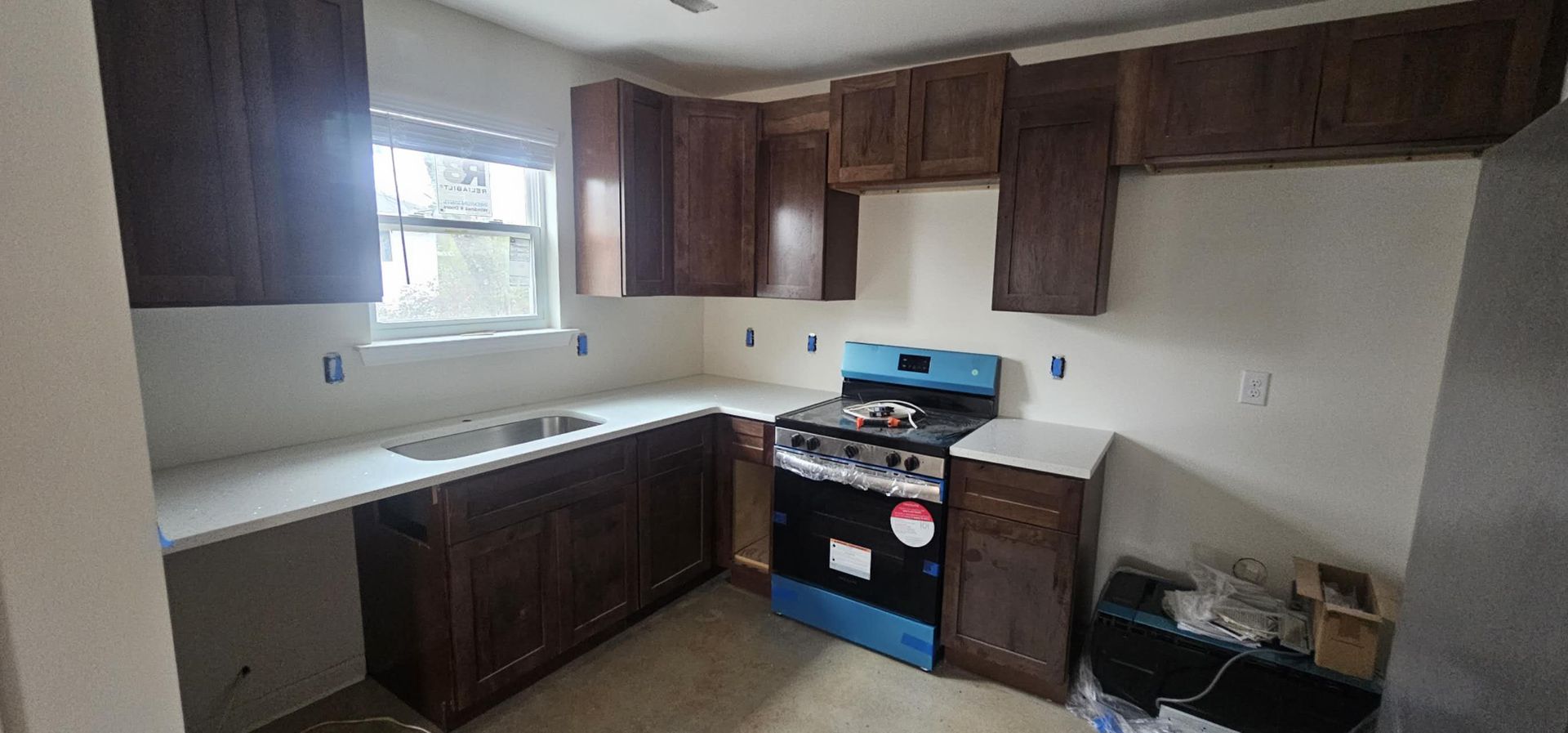 A kitchen with a stove, sink, cabinets, and a window.