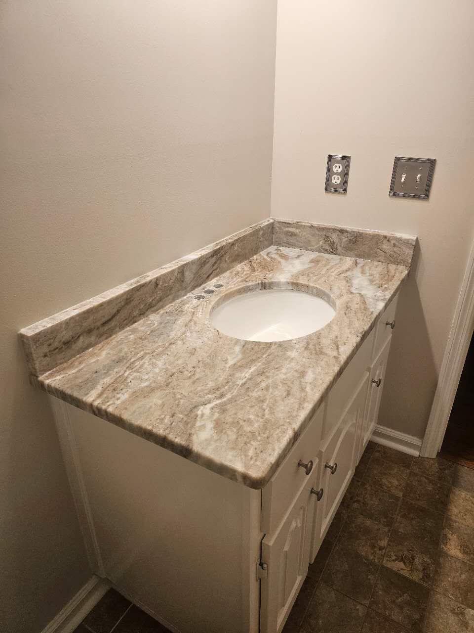 A bathroom vanity with a sink and a marble counter top.