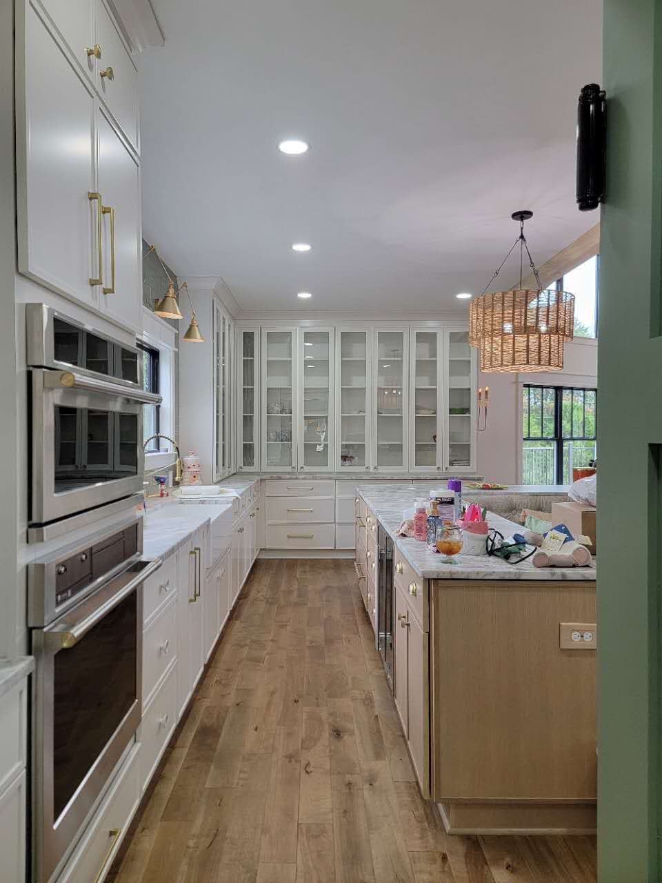 A kitchen with white cabinets, wooden floors, stainless steel appliances, and a large island.