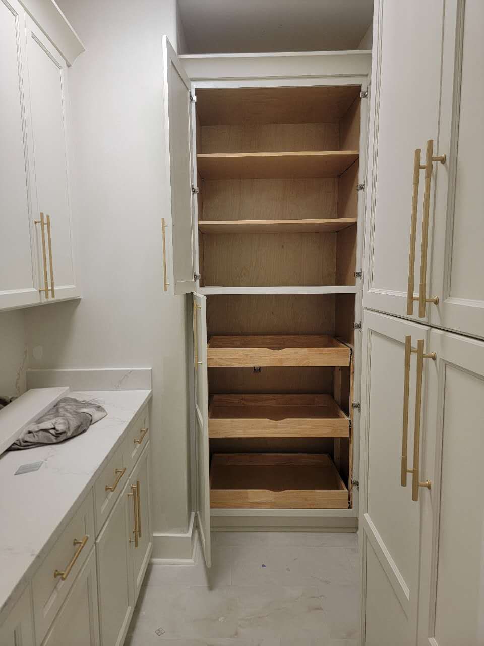 A kitchen with white cabinets and wooden shelves and drawers.