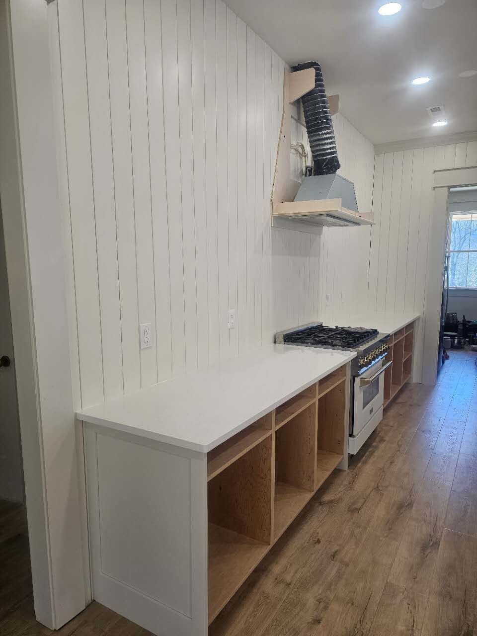 A kitchen with white cabinets, wooden floors, a stove and a hood.