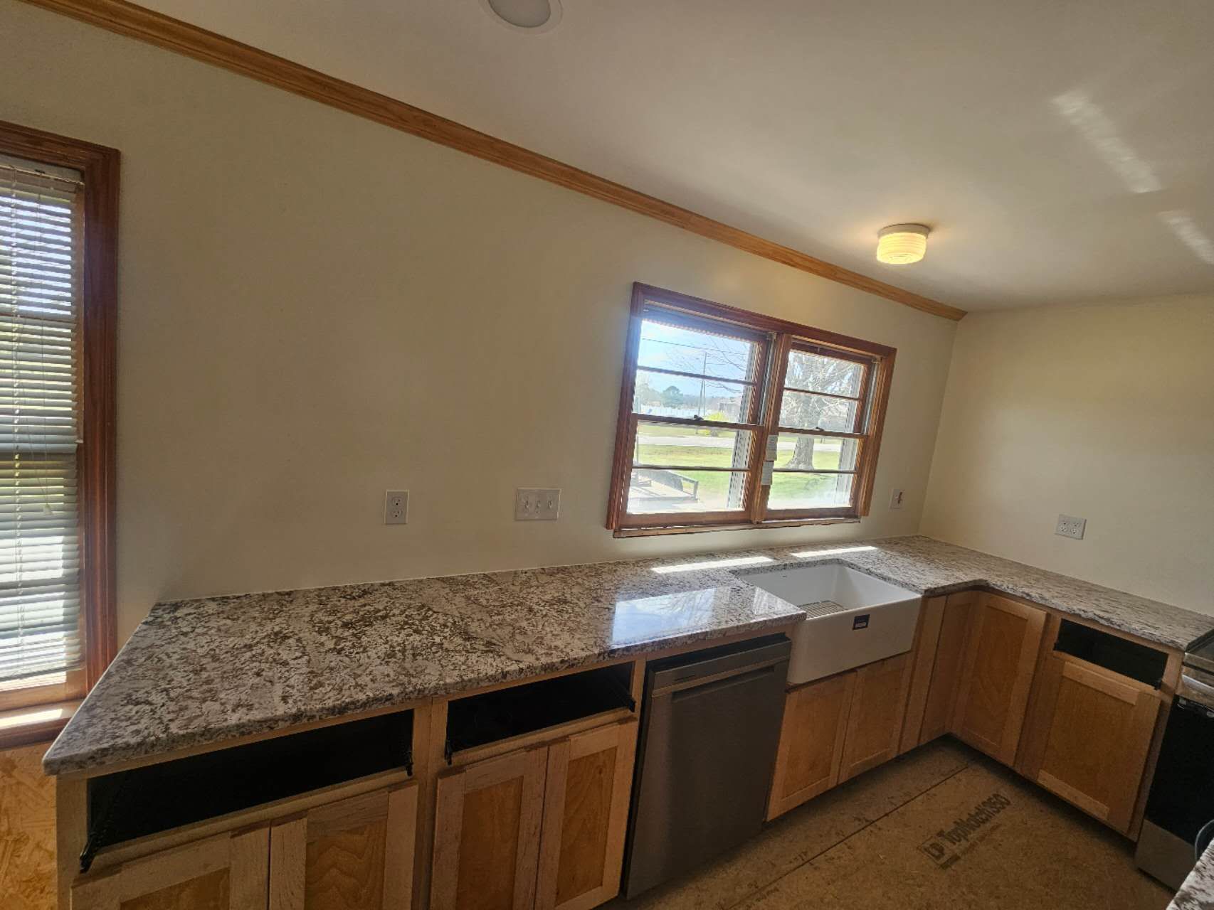 A kitchen with granite counter tops, wooden cabinets, a sink, and a dishwasher.