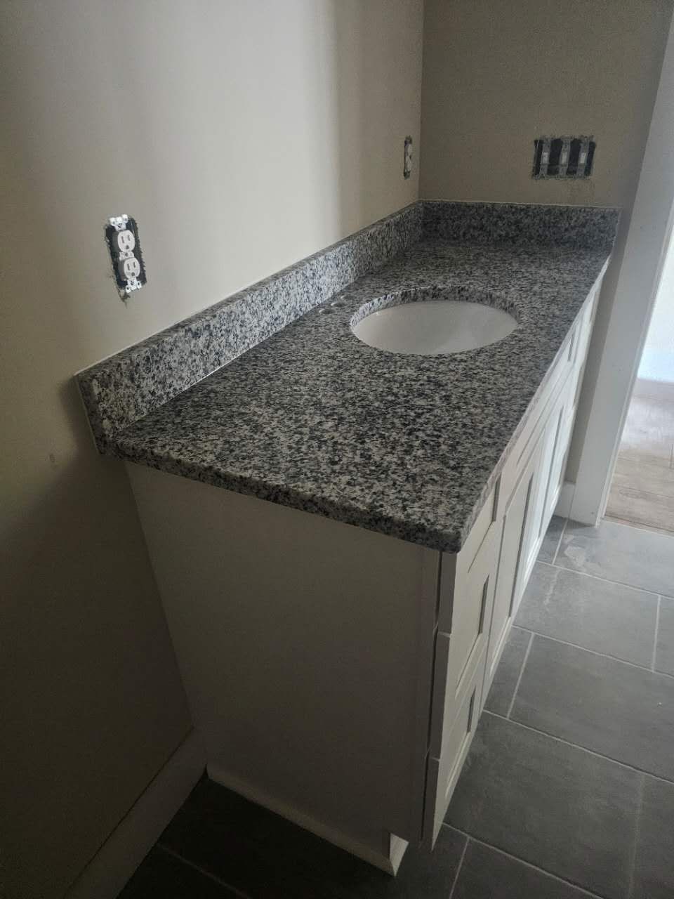 A bathroom vanity with a granite counter top and a sink.
