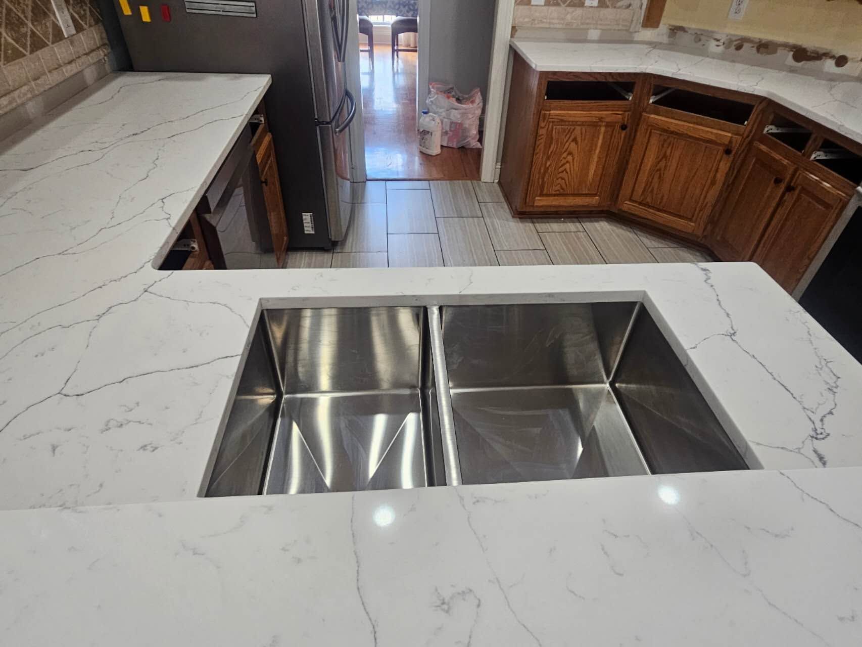 A kitchen with a stainless steel sink and white counter tops.