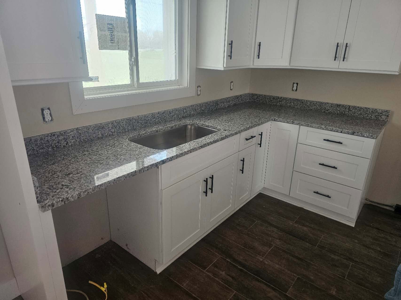 A kitchen with granite counter tops, white cabinets, and a sink.