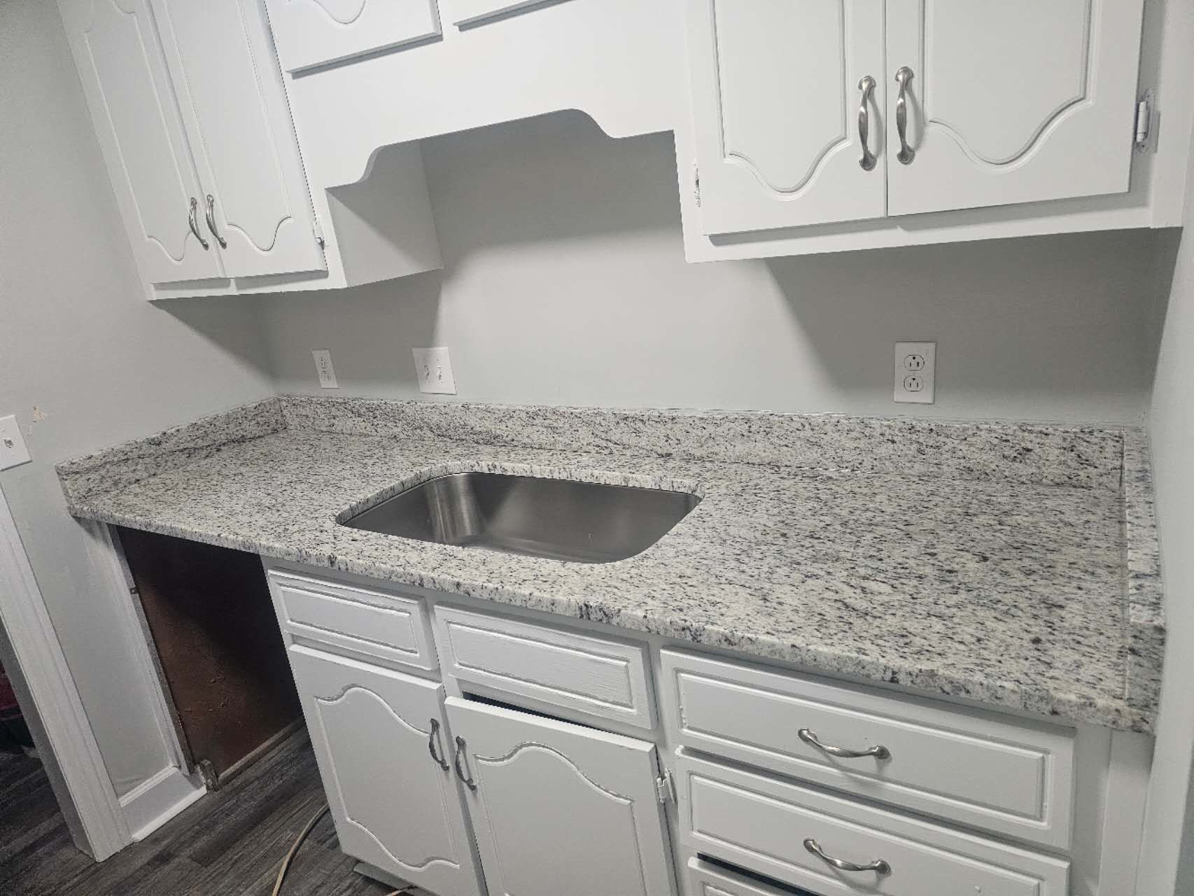 A kitchen with white cabinets and granite counter tops and a sink.