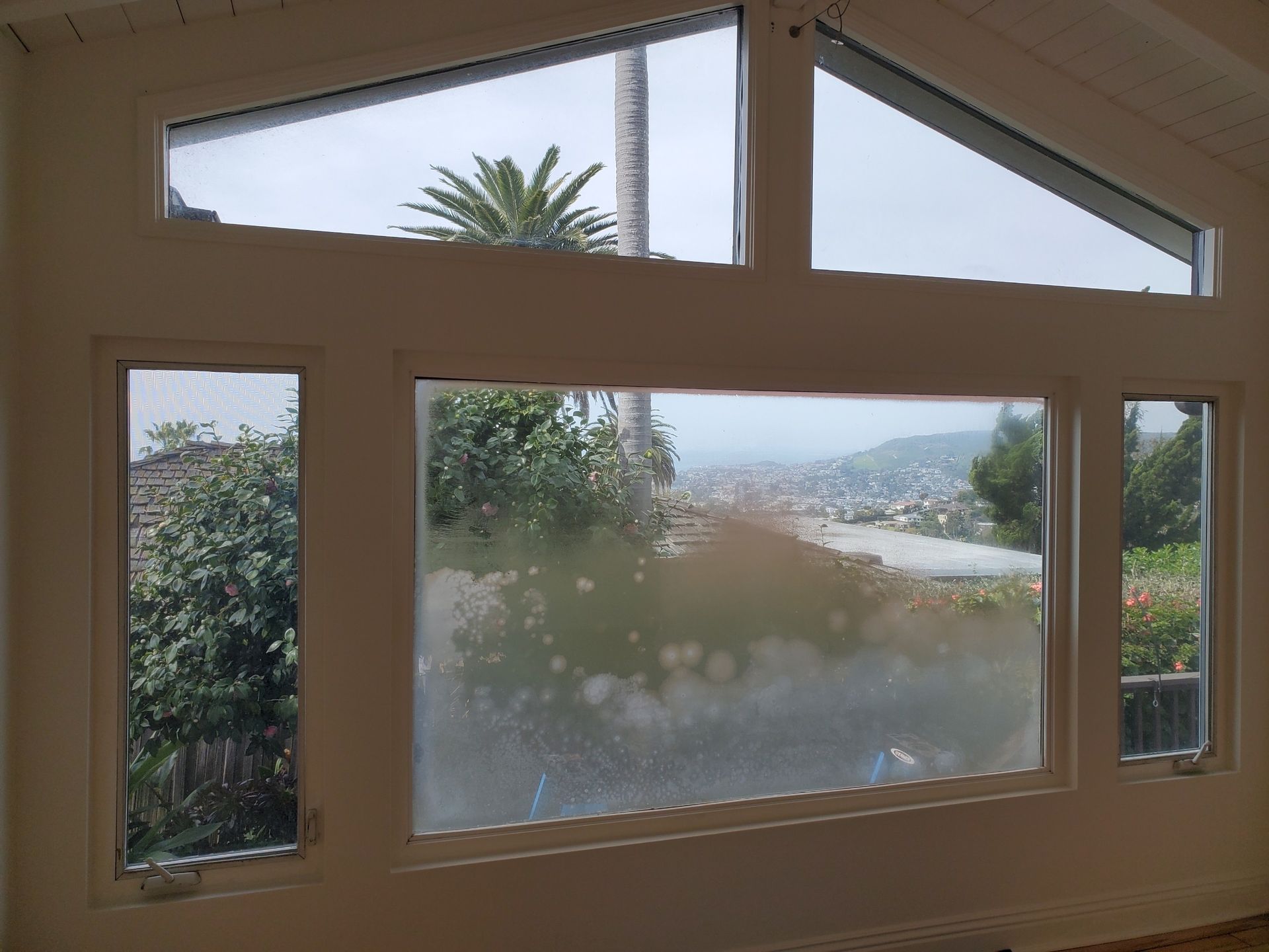 Windows with frosted glass, overlooking a cityscape and vegetation, inside a white-walled room.