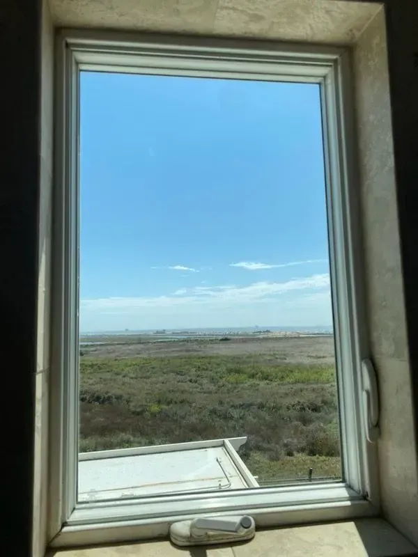 View through a window of a green landscape under a bright blue sky.
