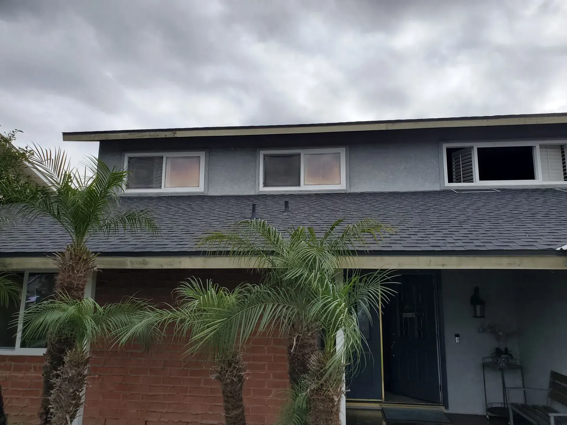 A two-story house with a brick facade and palm trees under a cloudy sky.