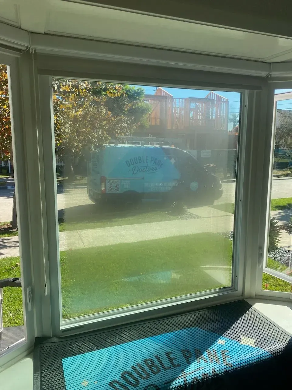 A view through a window of a grassy yard, a van with text, and trees under a bright sky.