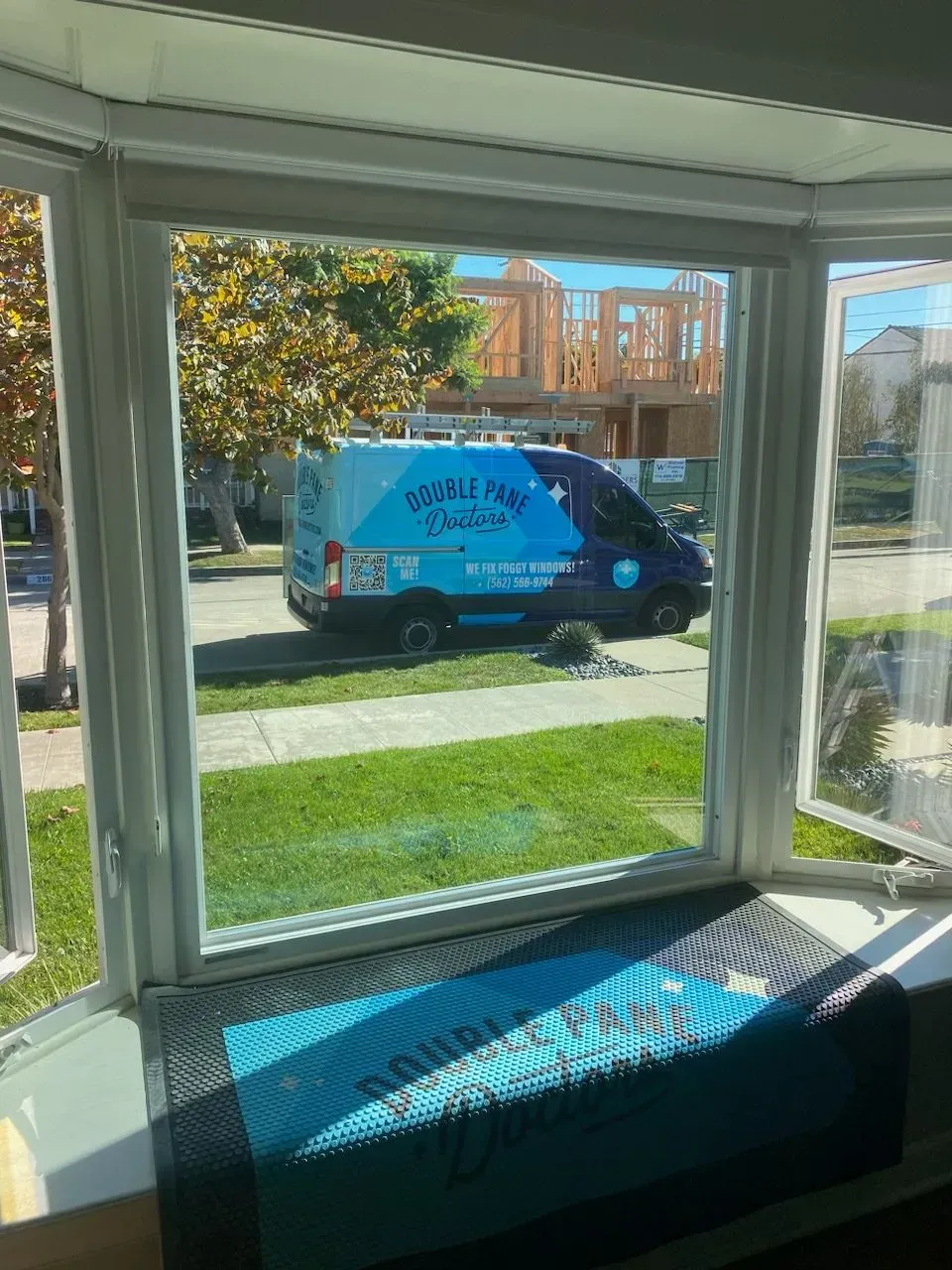 View through a window: a service van parked on a lawn, and a house under construction in the background.