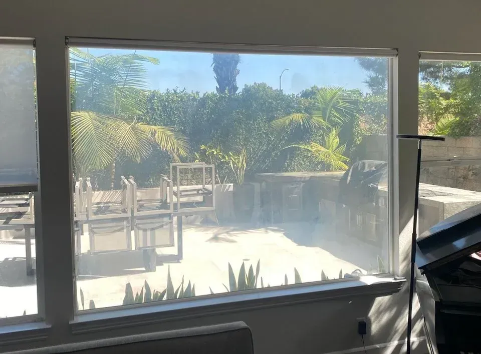 View through a window of an outdoor patio with chairs and greenery.