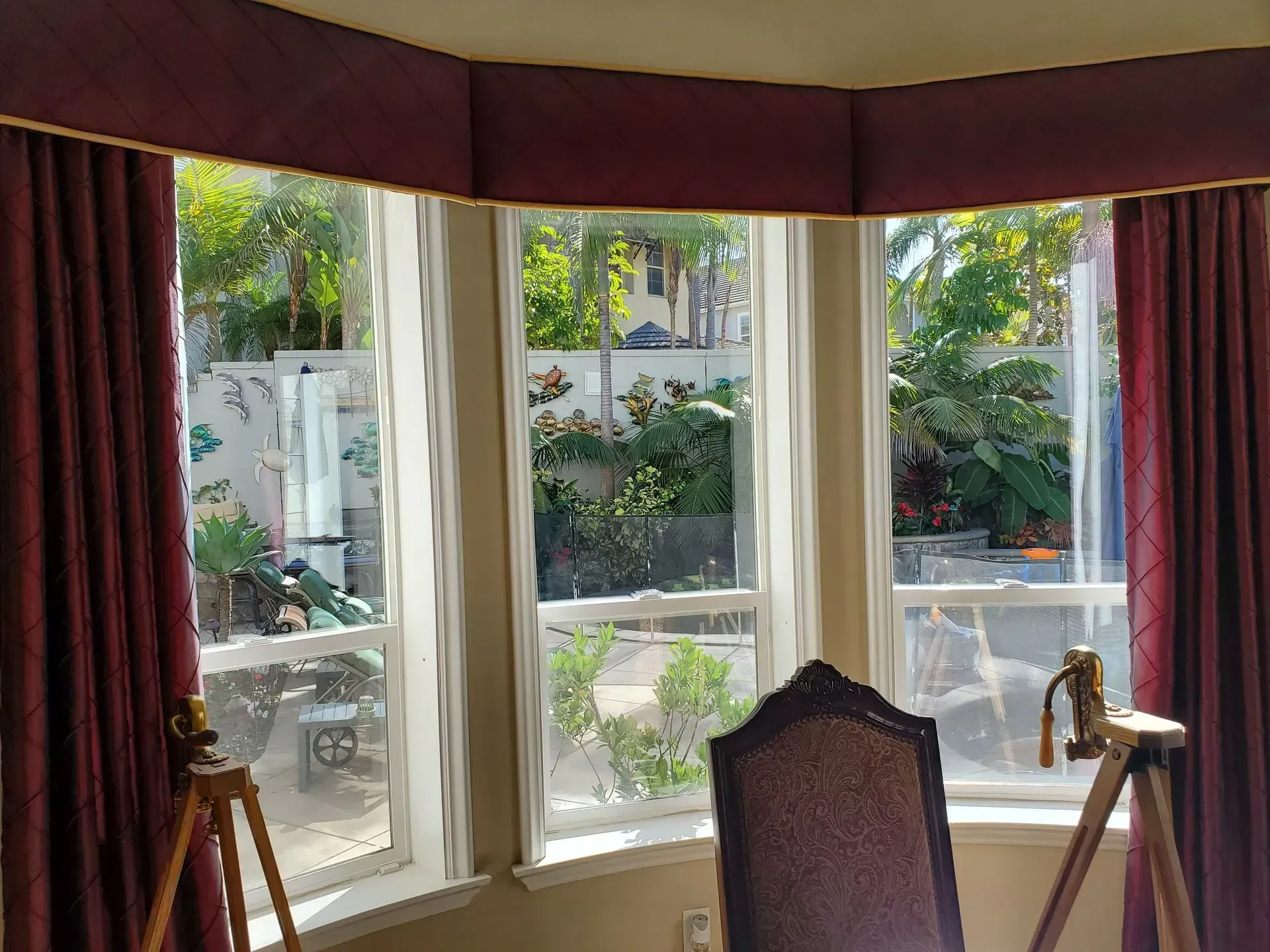 Bay window with burgundy drapes and valance overlooking a lush backyard.