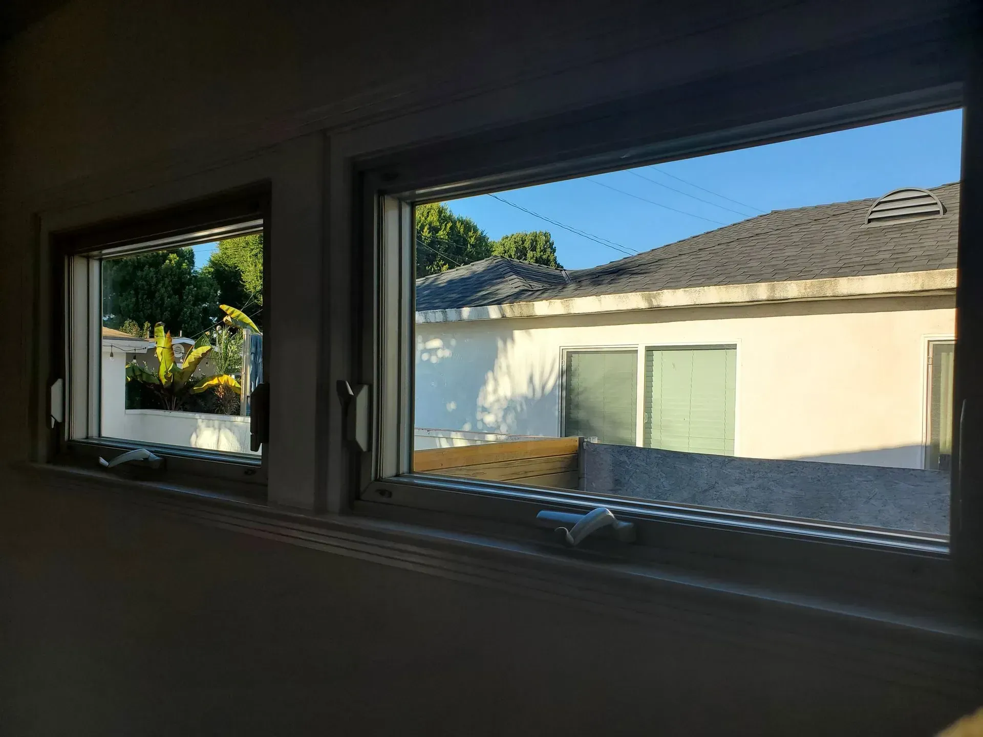 Two open windows reveal a sunny outdoor scene with a white building, trees, and blue sky.