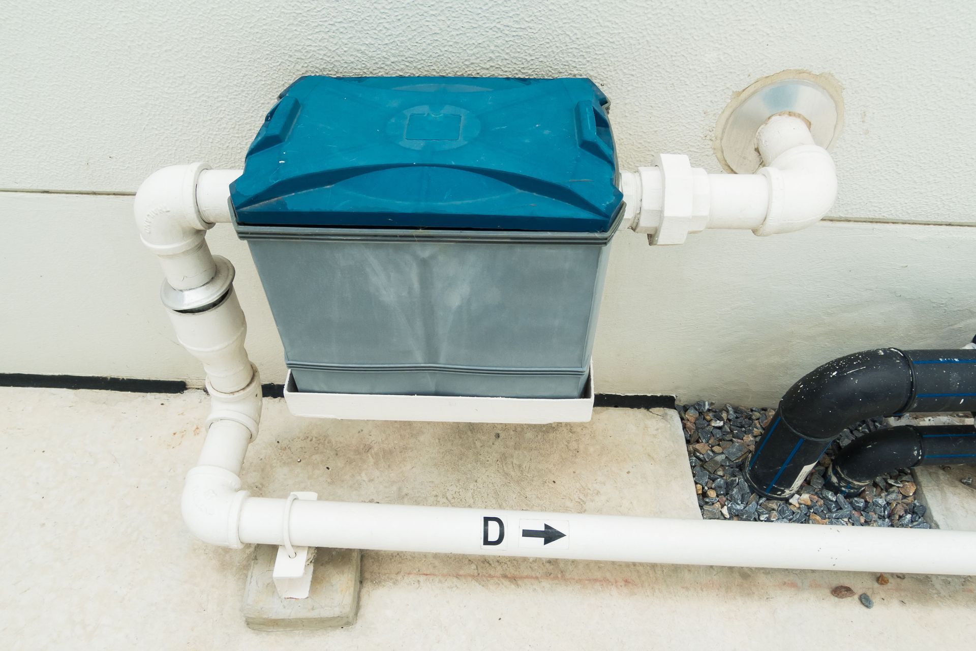 A gray filter with a blue lid, connected to white pipes, mounted on a wall.