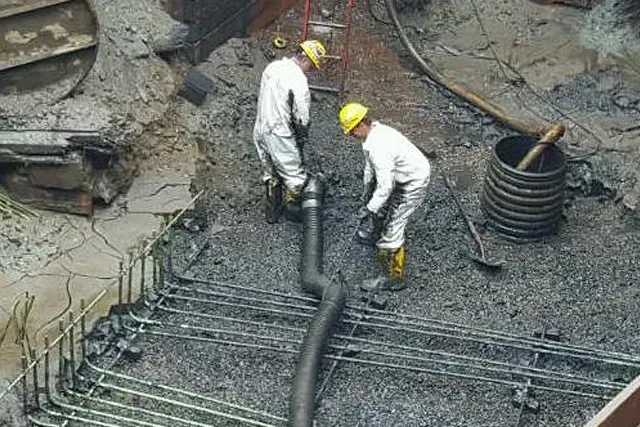 Two workers in protective suits connect a large hose in a construction site.