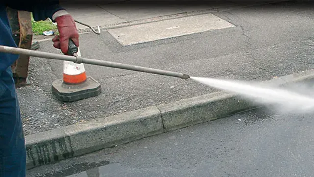 Person with red glove uses a pressure washer to clean a sidewalk and curb.