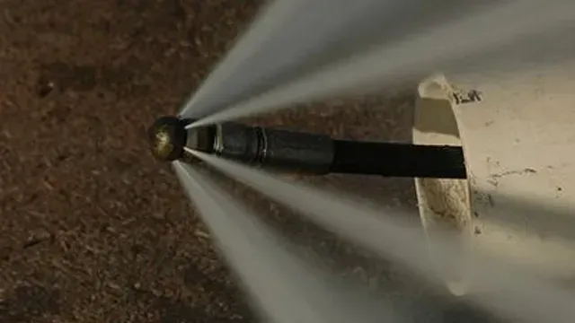 Water jet blasting from a nozzle inside a white pipe, clearing debris.