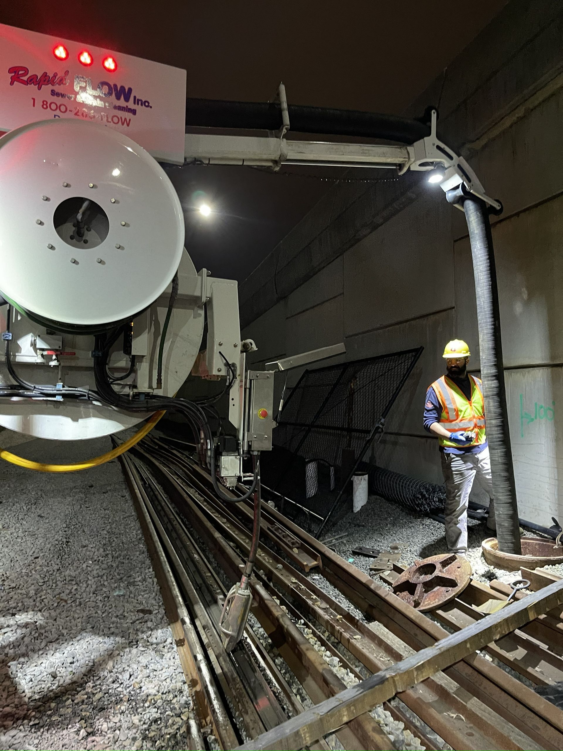 A machine working on a subway track with a worker in a safety vest.