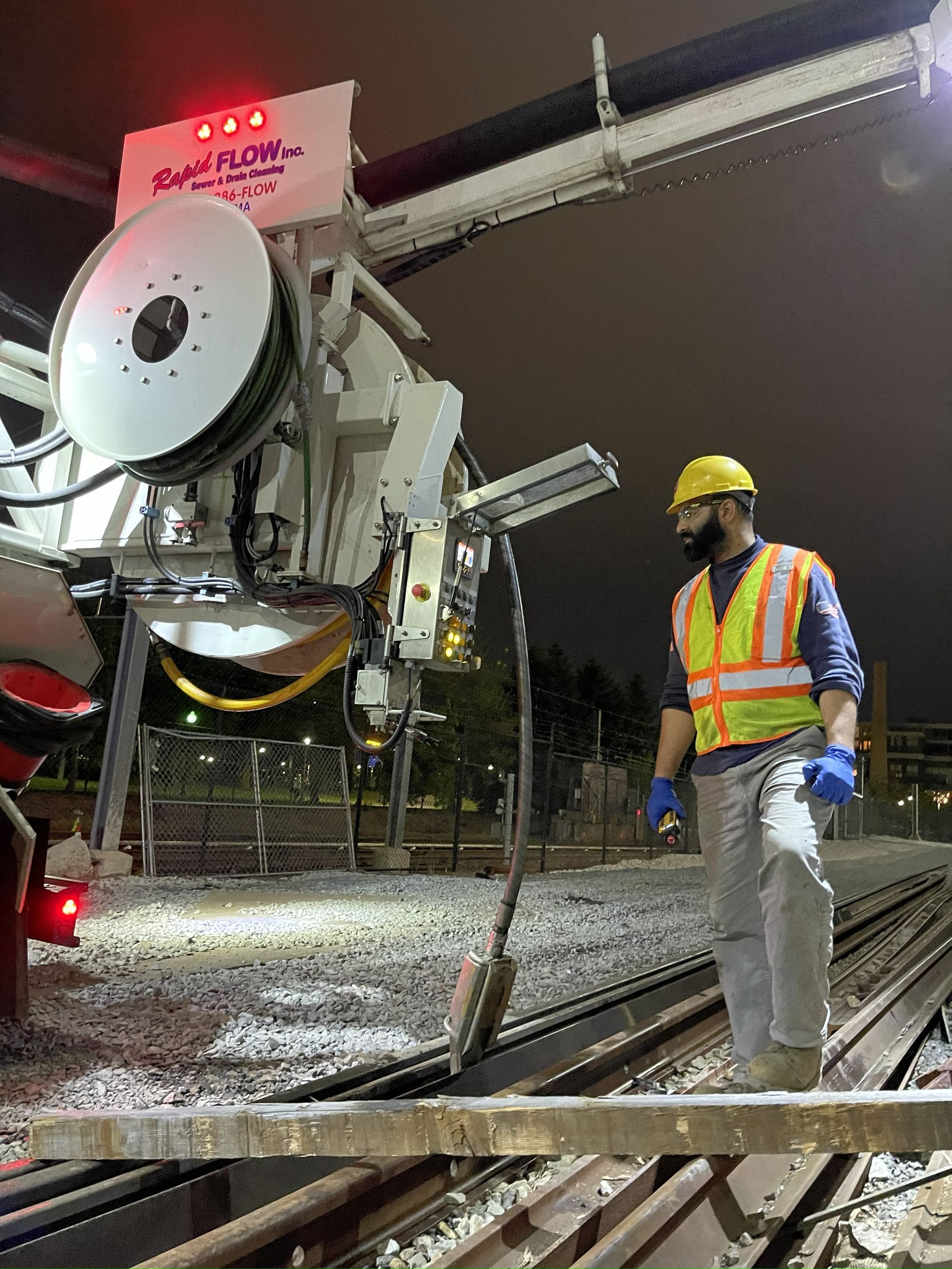 Worker in safety vest, hard hat, and face mask standing by rail car on tracks at night.