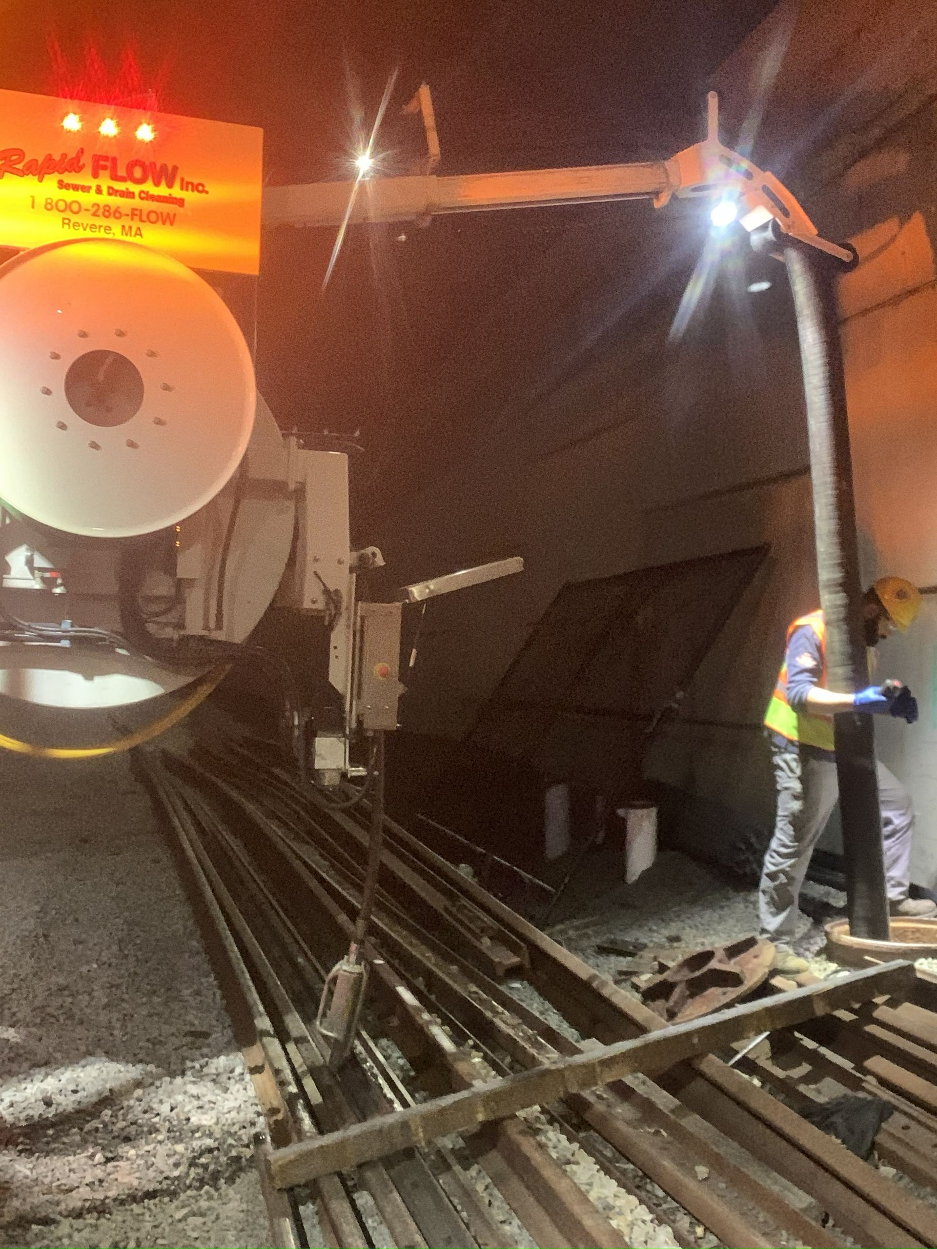 Workers in a tunnel use machinery to work on tracks. A large sign with lights is visible.