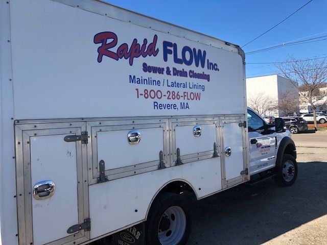 White Rapid Flow Inc. truck for sewer and drain cleaning, parked on a street with blue sky.
