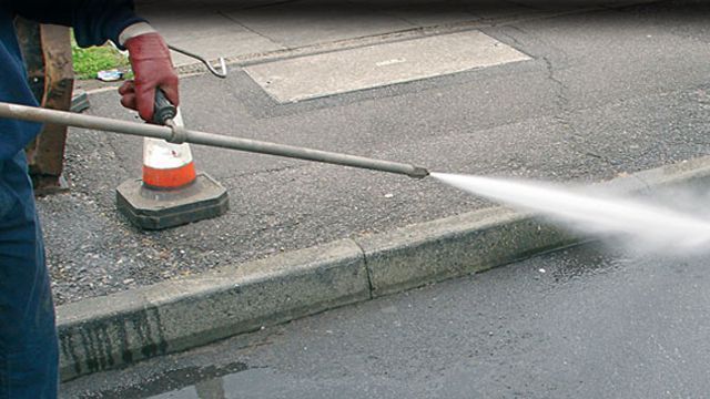 Person power washing a street curb with a pressure washer, creating a mist of water.